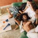 Three people sitting cosily on a green couch with Man.Wand Edgy steller blue lying on a table. 